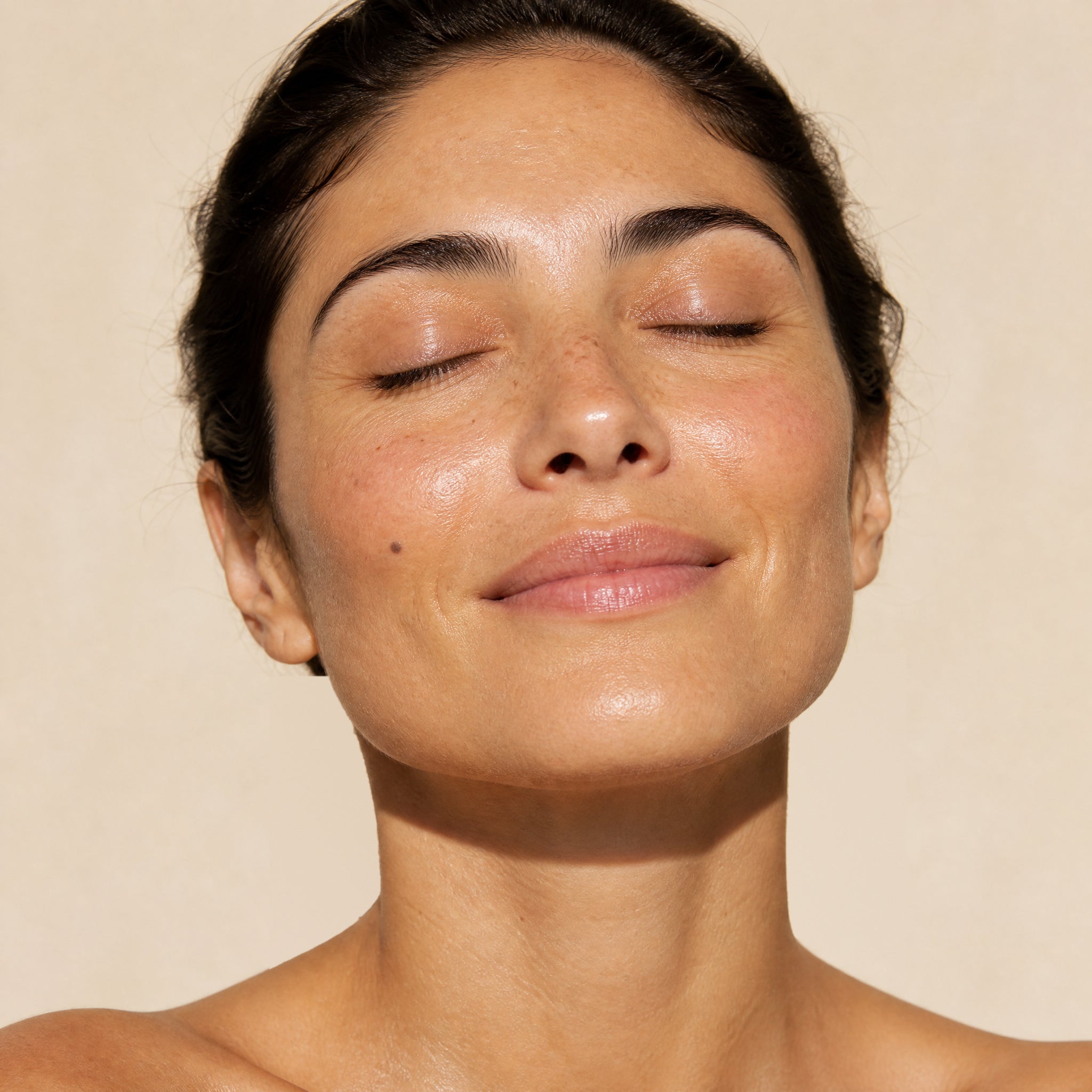 Close-up of a woman with her eyes closed and her face tilted up towards soft light, smiling gently
