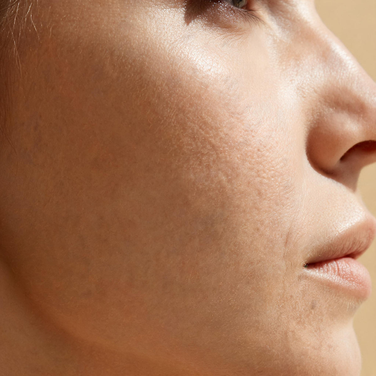 Luminous cheekbone lit against a warm champagne background - Skingenetix brightening and glow peptide range