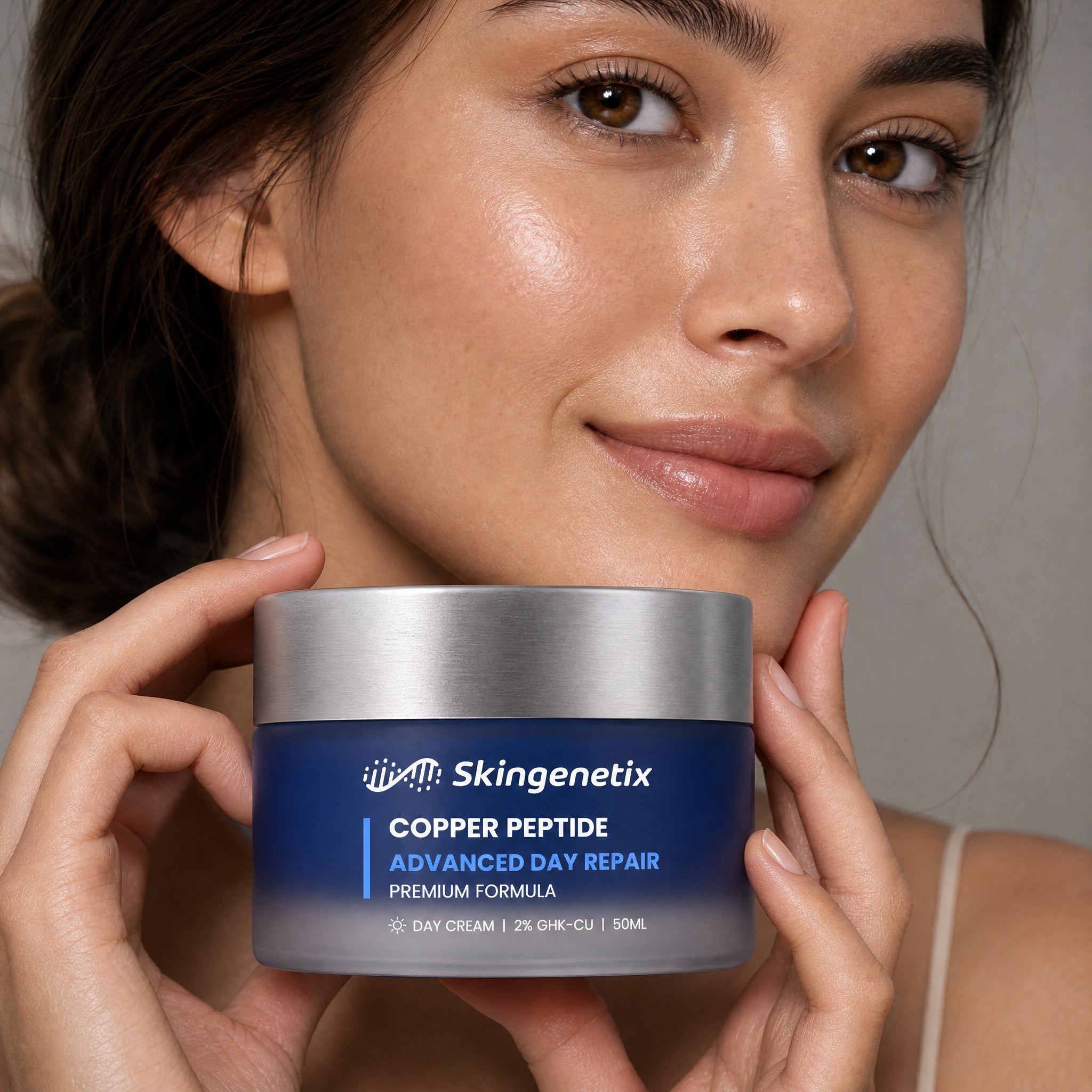 Woman holding a deep blue frosted glass jar of Skingenetix Copper Peptide Advanced Day Repair cream, 50ml, up beside her jaw