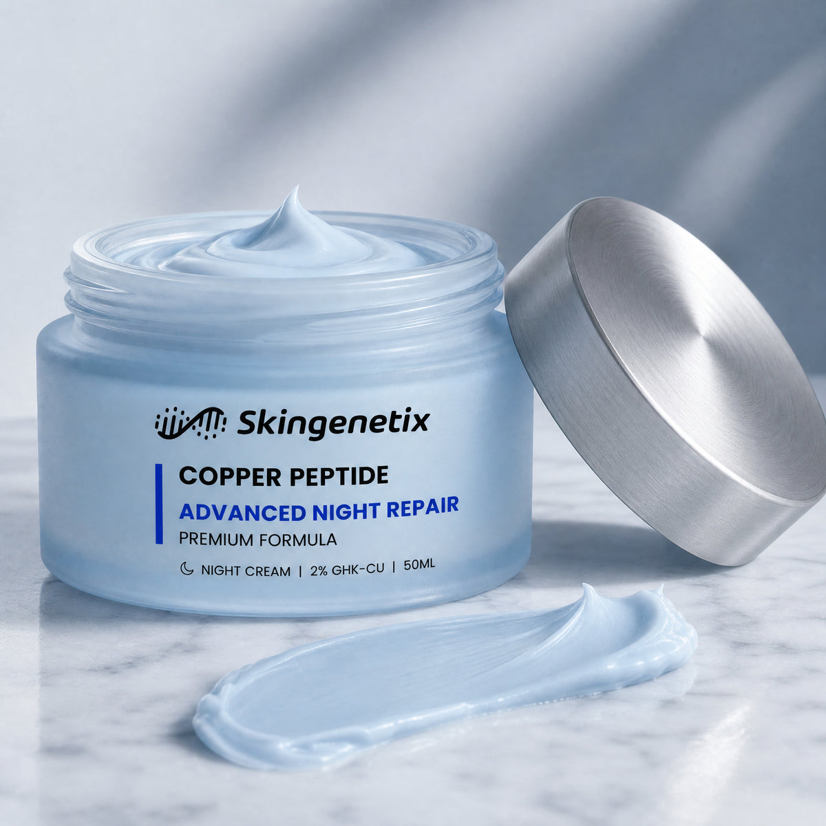 Open frosted glass jar of Skingenetix Copper Peptide Advanced Night Repair cream, 50ml, on marble with the silver lid resting beside it and a swatch of pale blue cream in the foreground