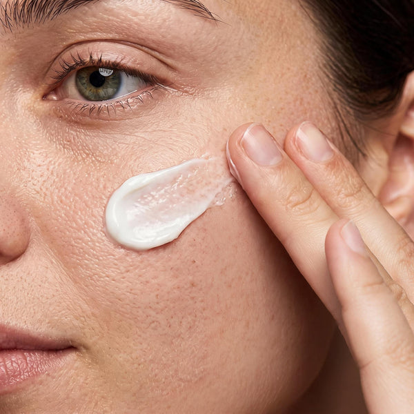 Close-up of a woman smoothing a swatch of cream into her cheek with her fingertips
