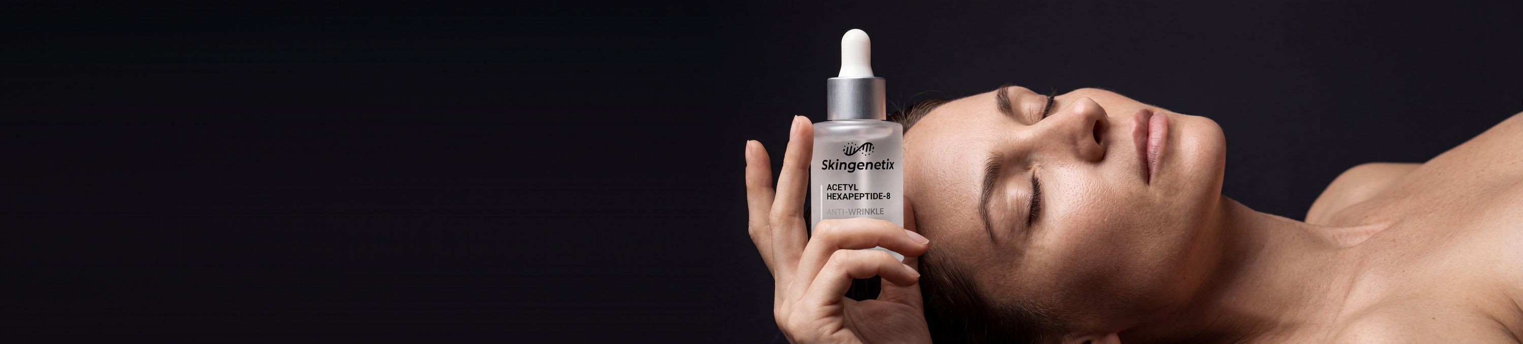 Woman reclining with her eyes closed, holding a bottle of Skingenetix Acetyl Hexapeptide-8 anti-wrinkle serum beside her face on a dark studio backdrop