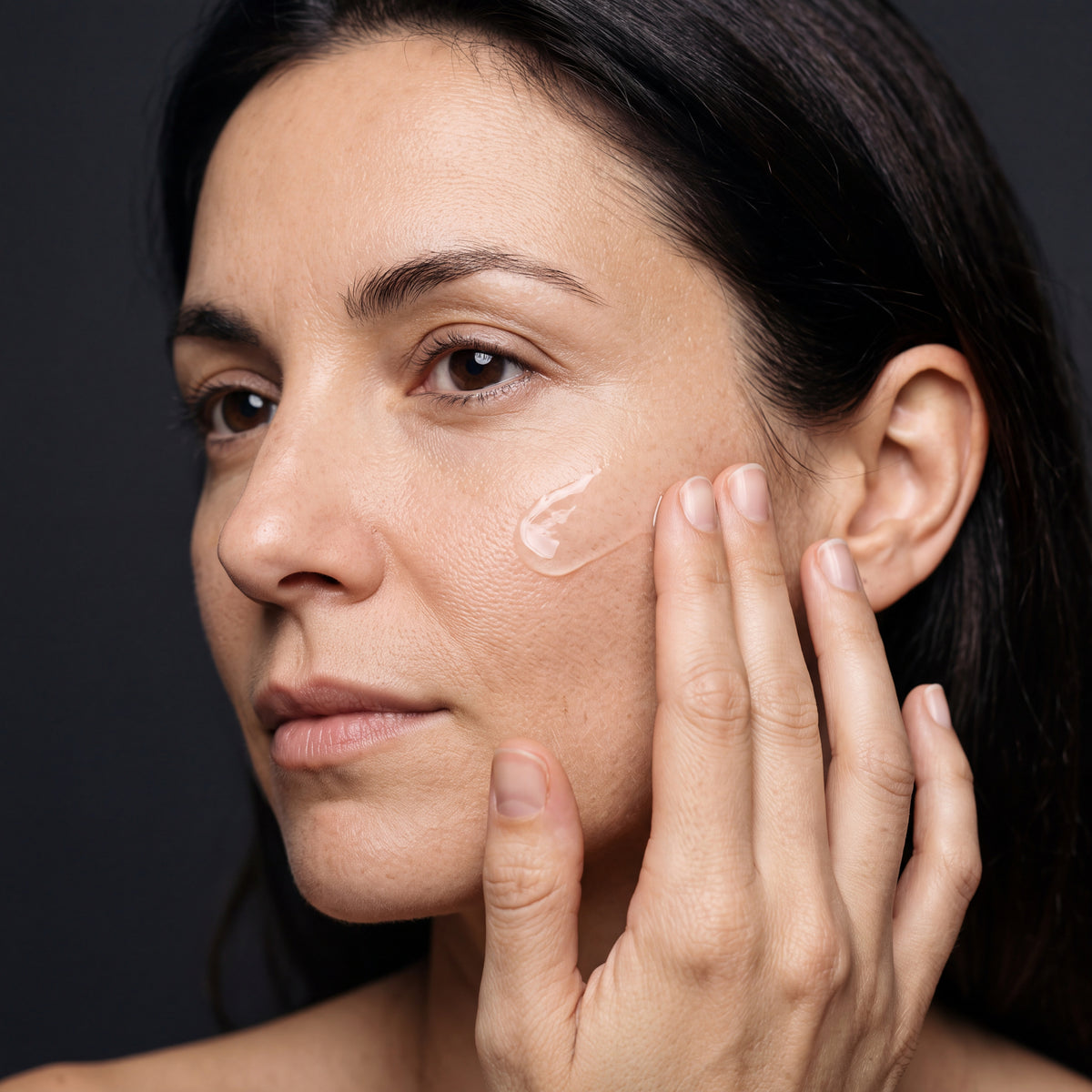 Woman applying a small amount of clear serum to her cheekbone with her fingertips