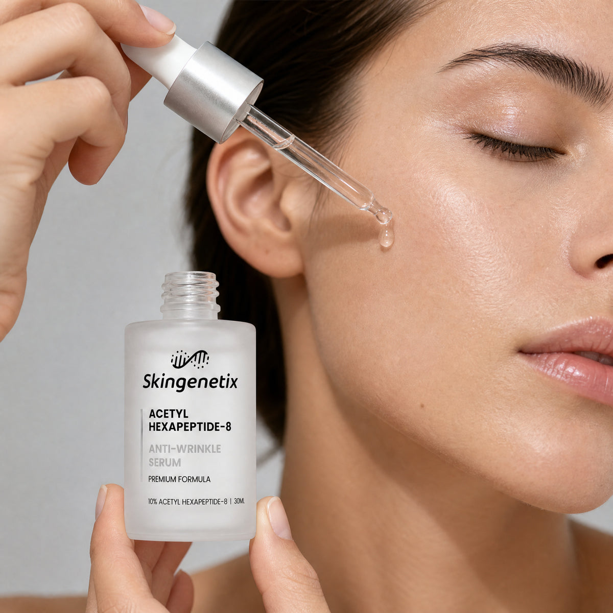 Close-up of a woman with her eyes closed holding a 30ml frosted glass bottle of Skingenetix Acetyl Hexapeptide-8 Anti-Wrinkle Serum and releasing a drop from the glass dropper beside her cheek