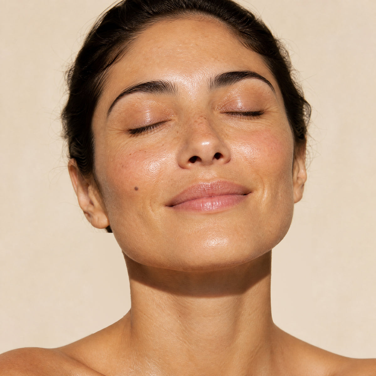 Close-up of a woman with her eyes closed and her face tilted up towards soft light, smiling gently