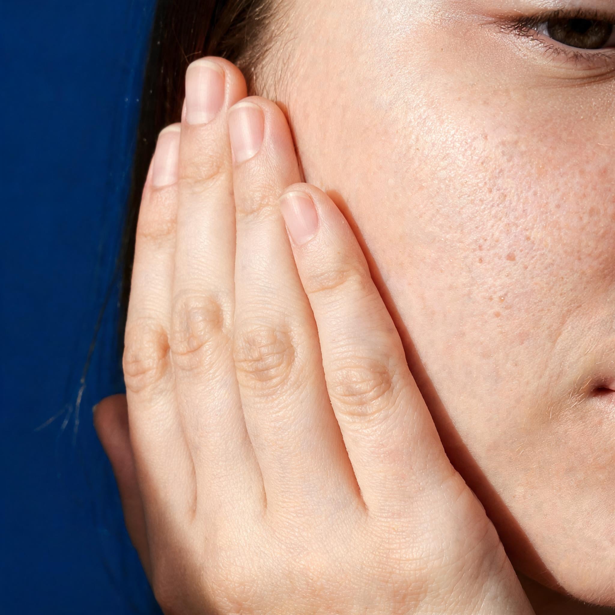A hand resting against the cheek against a clinical blue background - Skingenetix skin repair and renewal peptide range