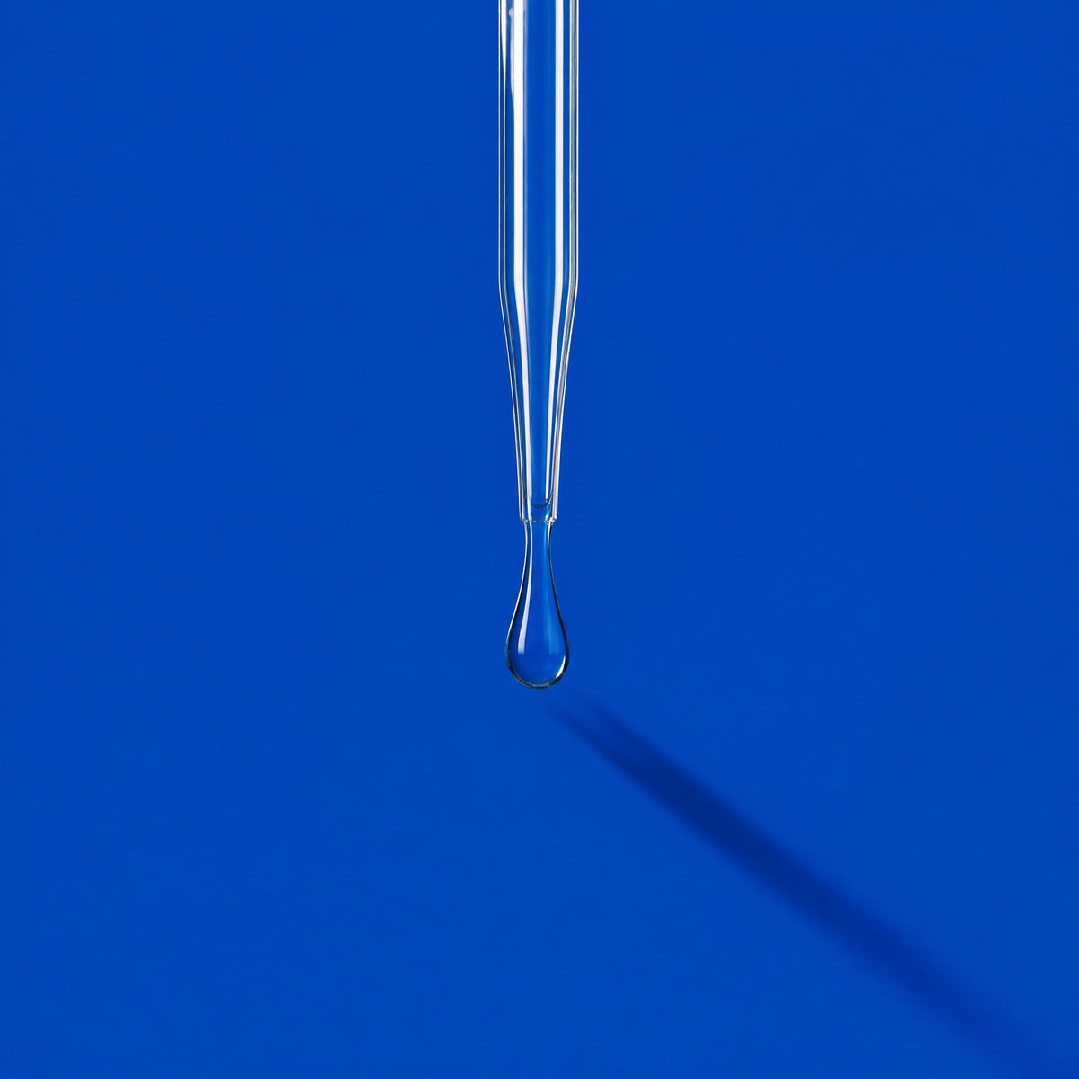 A glass pipette releasing a droplet on a clinical blue ground