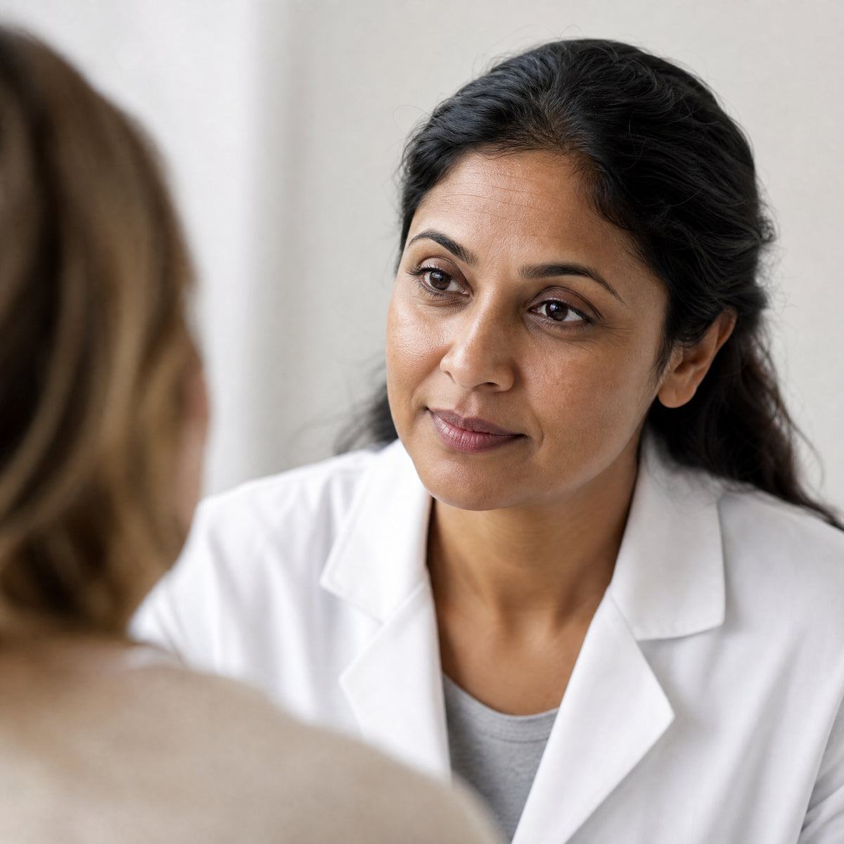 A dermatologist in a white coat listening to a client during a skin consultation