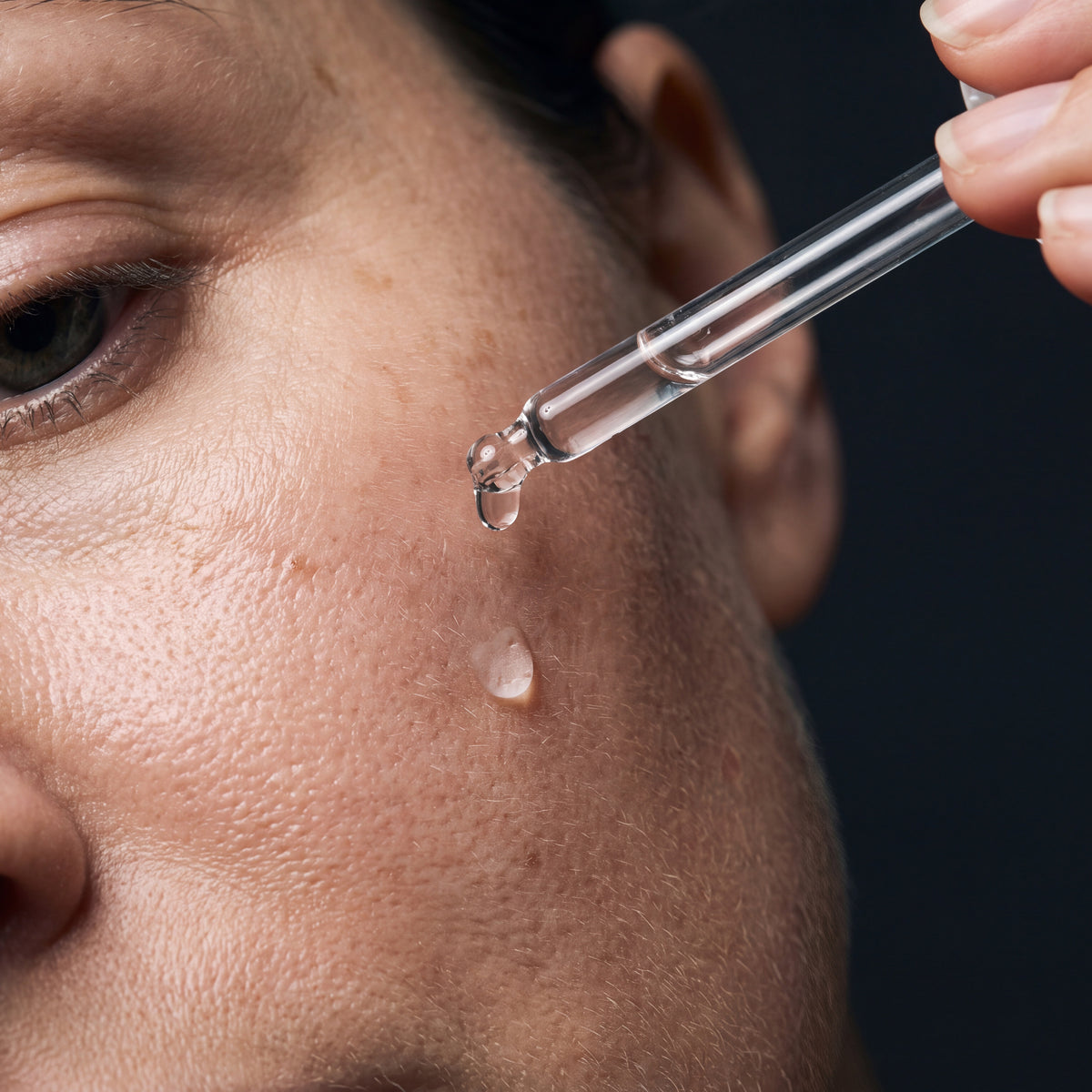 Skingenetix Full Matrixyl 3000 Ritual - Serum & Cream - a dropper releasing a clear drop of the firming serum onto a cheek