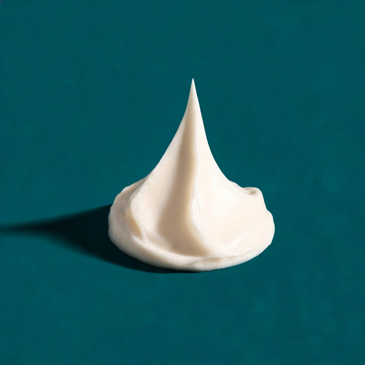 A soft peak of white moisturiser on a deep teal surface