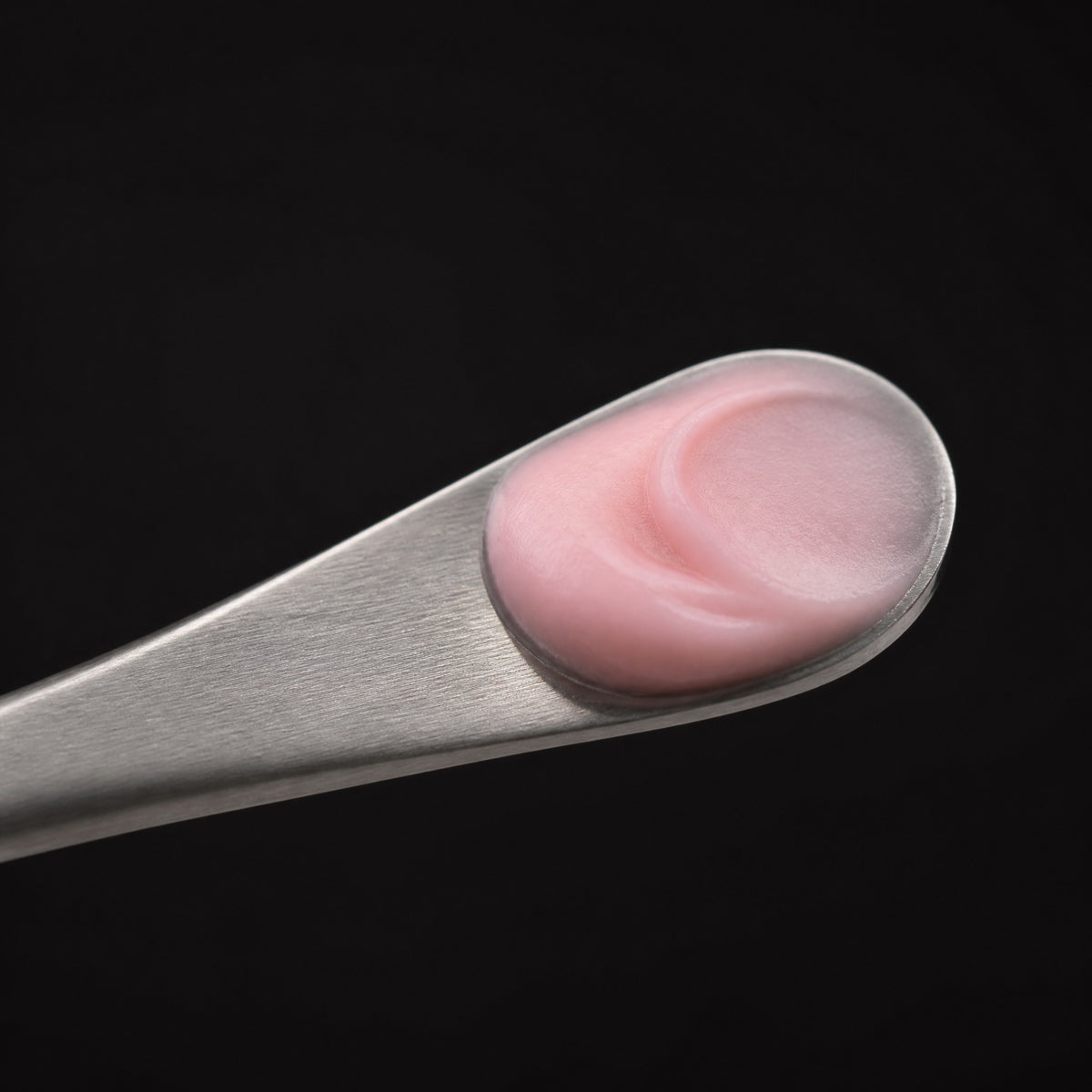 A steel spatula holding pink PDRN cream