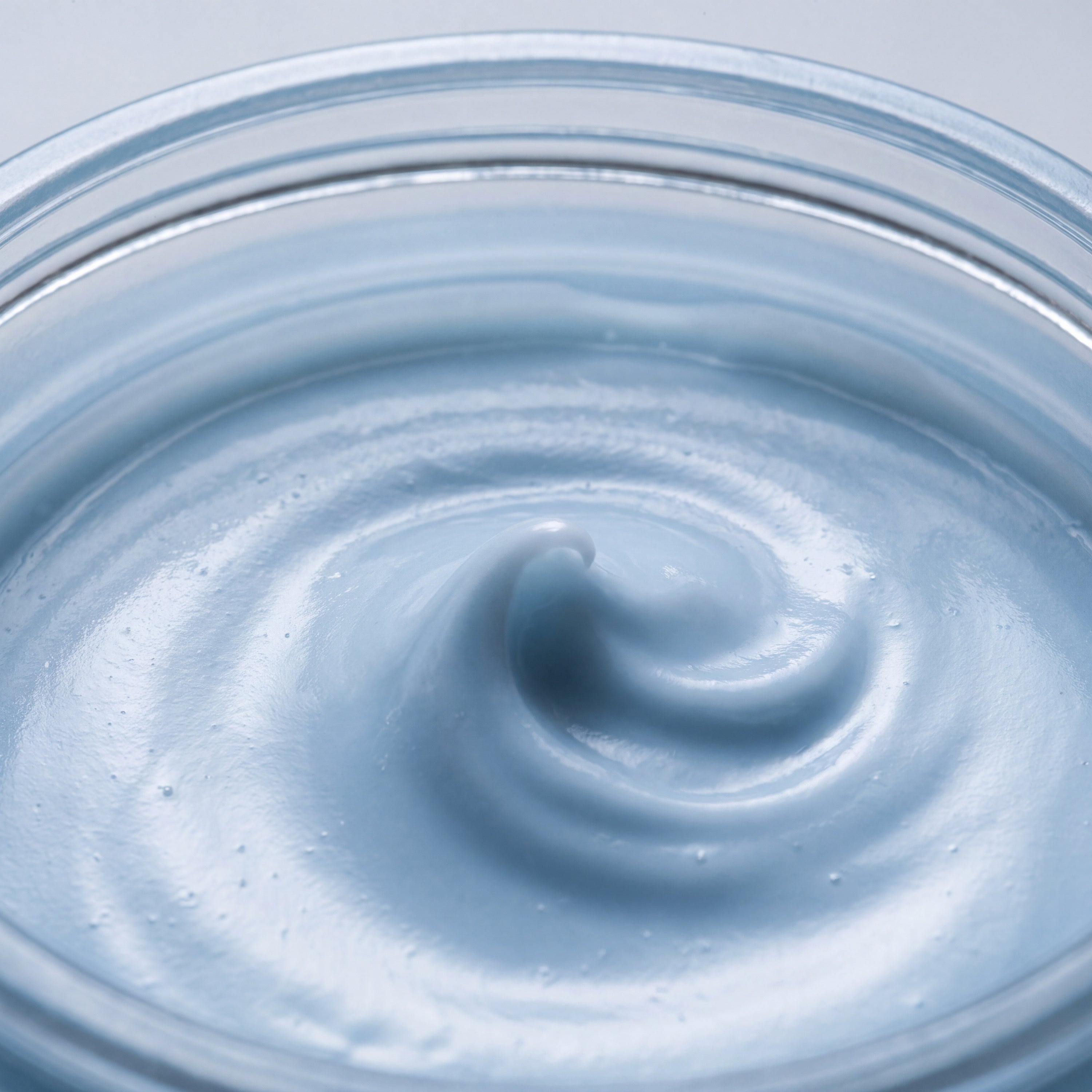 Macro close-up of a pale blue cream swirled to a soft peak in a glass jar, showing its smooth even texture