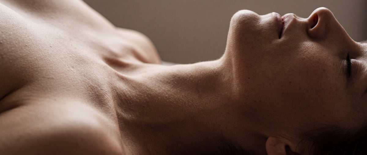 Close-up of a reclining woman's shoulder, throat and jaw lit softly against a warm neutral backdrop